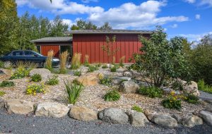 landscaping including various grasses and shrubs spaced out in front of red house